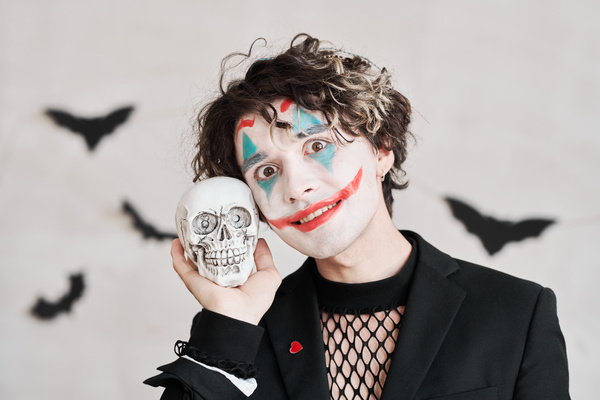 Man with Joker Makeup and Skull near His Face Smiles Ominously